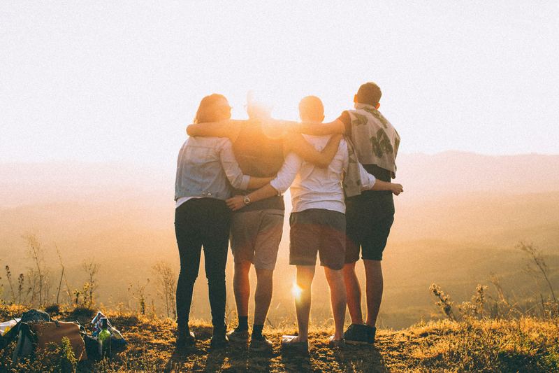 Four friends with arms around each other at sunset