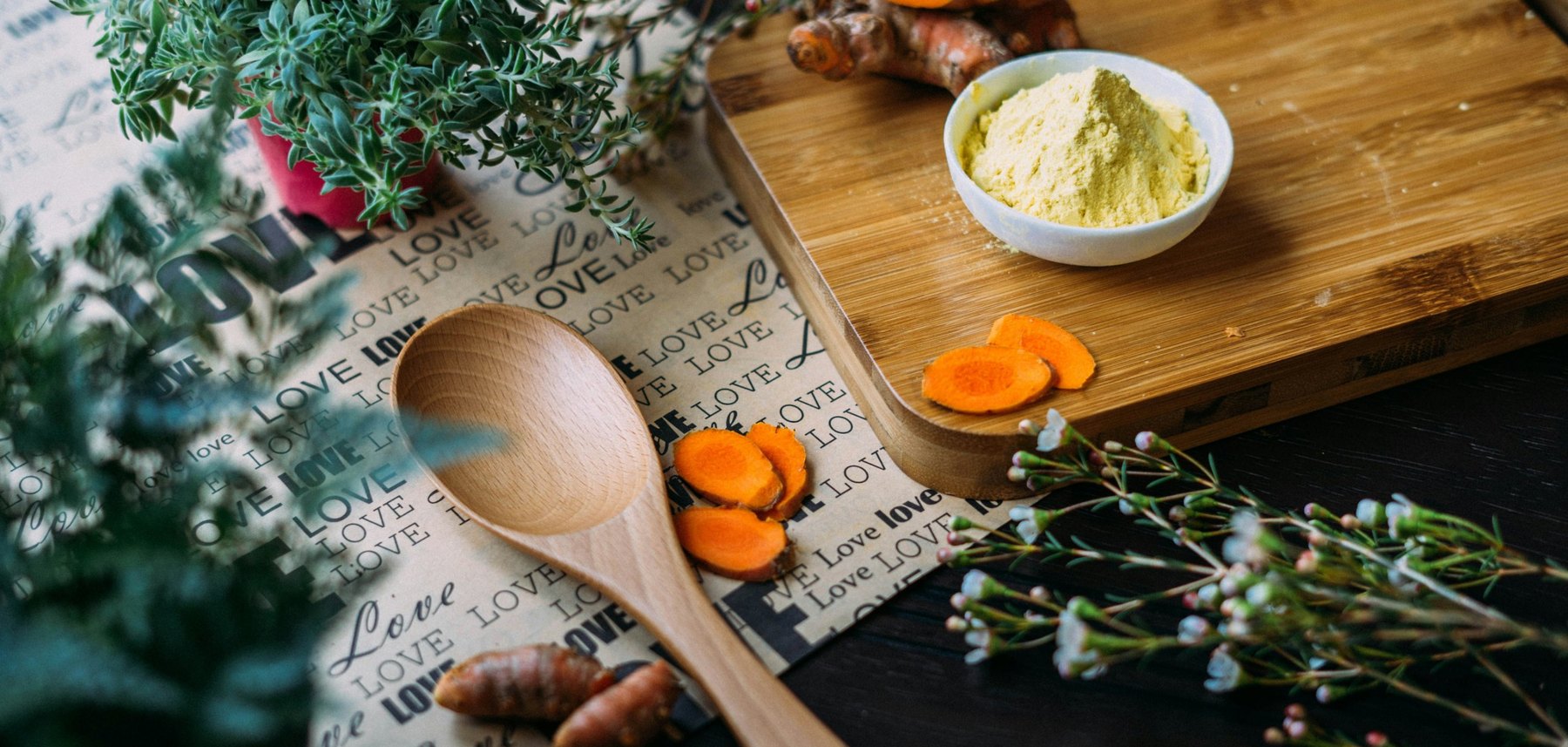 Fresh turmeric root, sliced turmeric and a bowl of ground spice beside a wooden spoon and cutting board