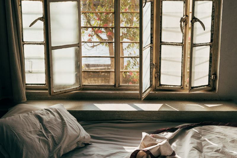 Unmade bed beside an open window